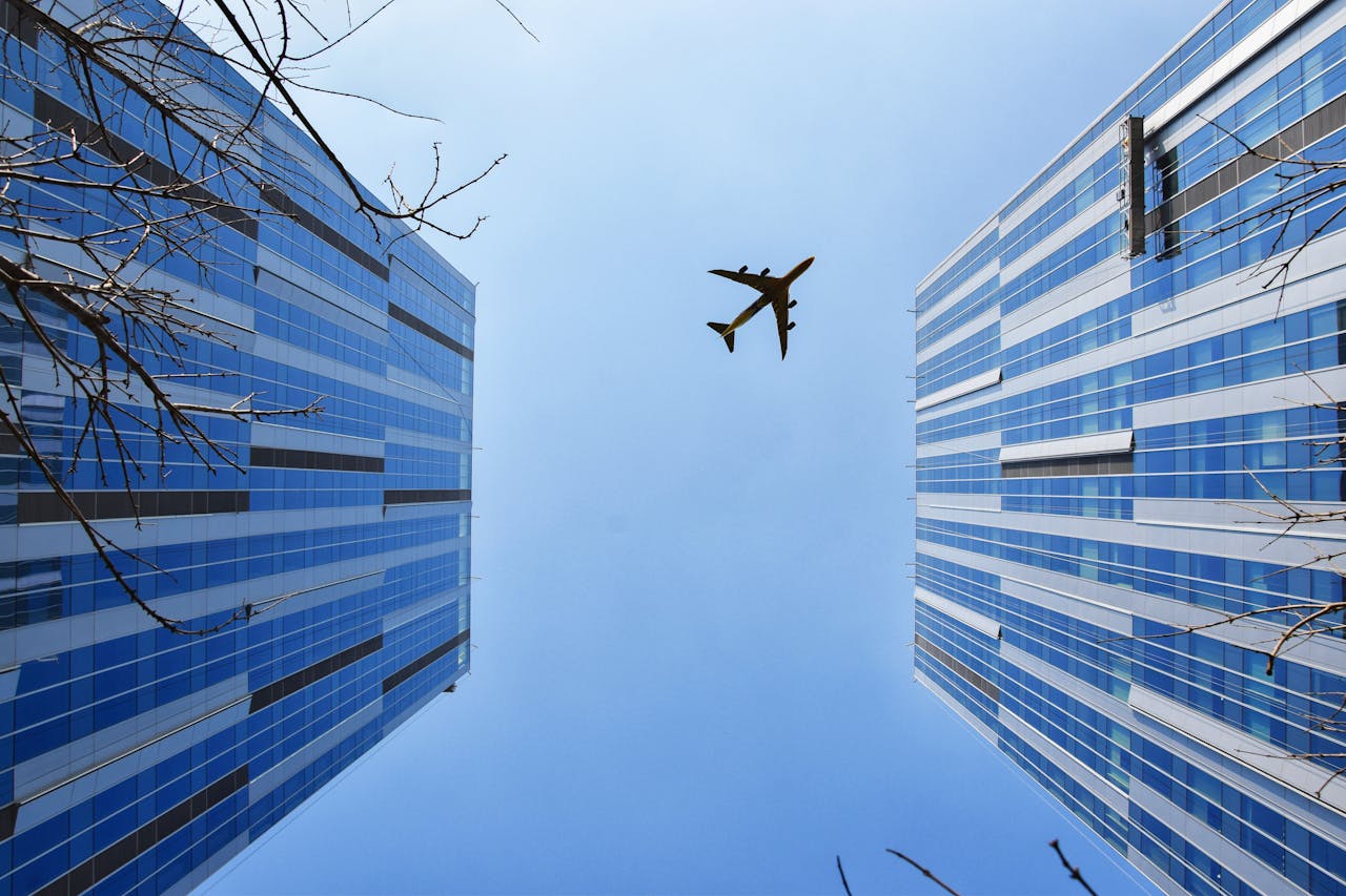 Two city buildings side by side with a plane flying over them